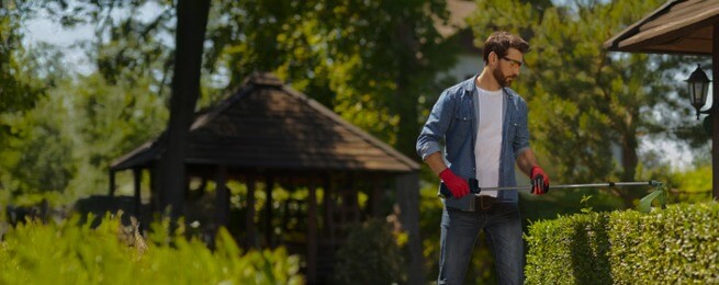A man using maxreach tools to trim a bush